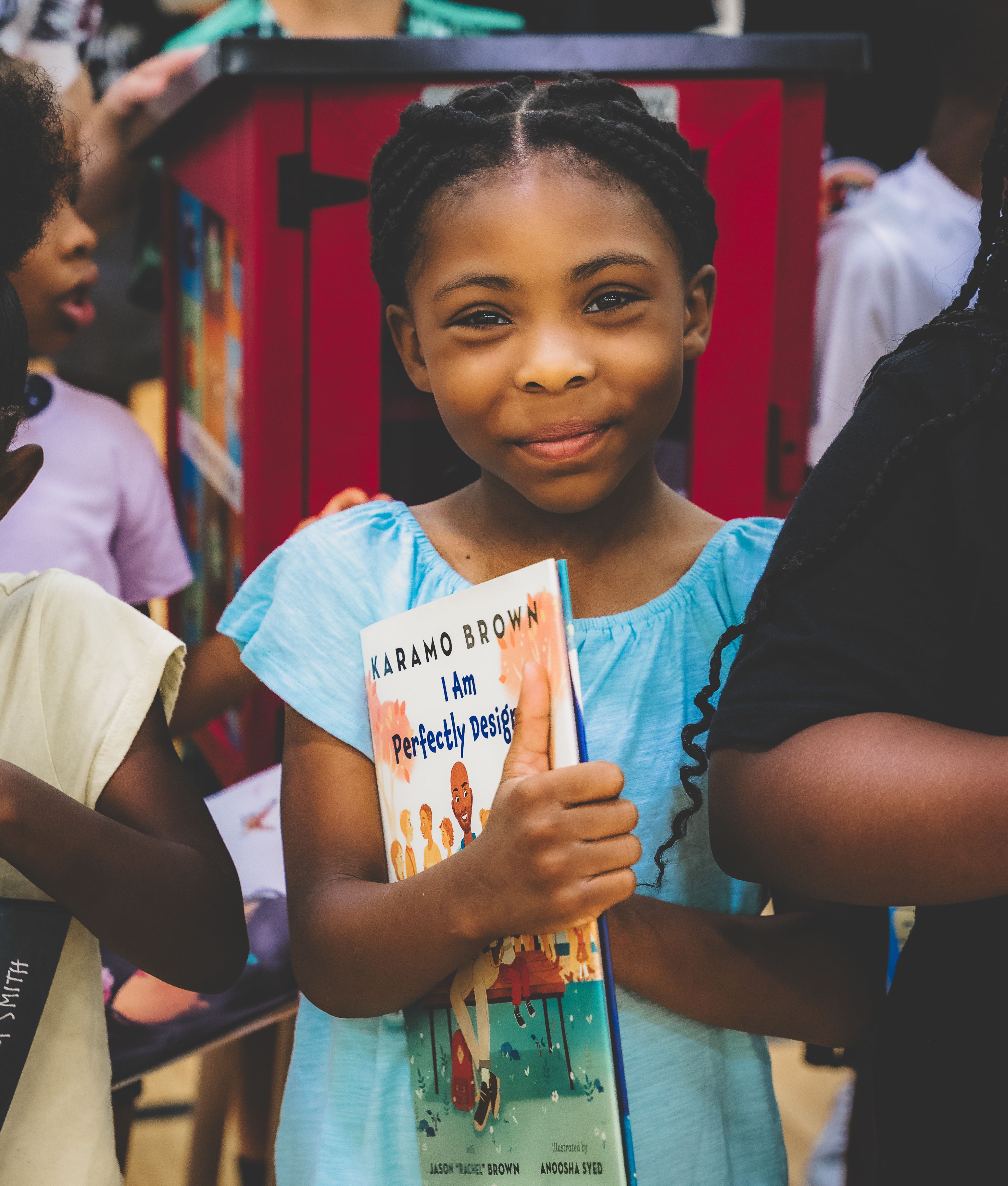 Child holding book in front of Little Free Library.